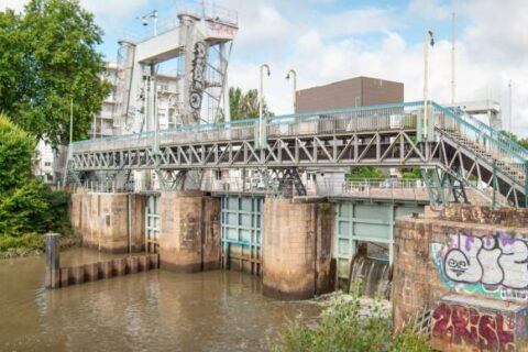A metal dam spans over a river with graffiti on nearby stone supports
