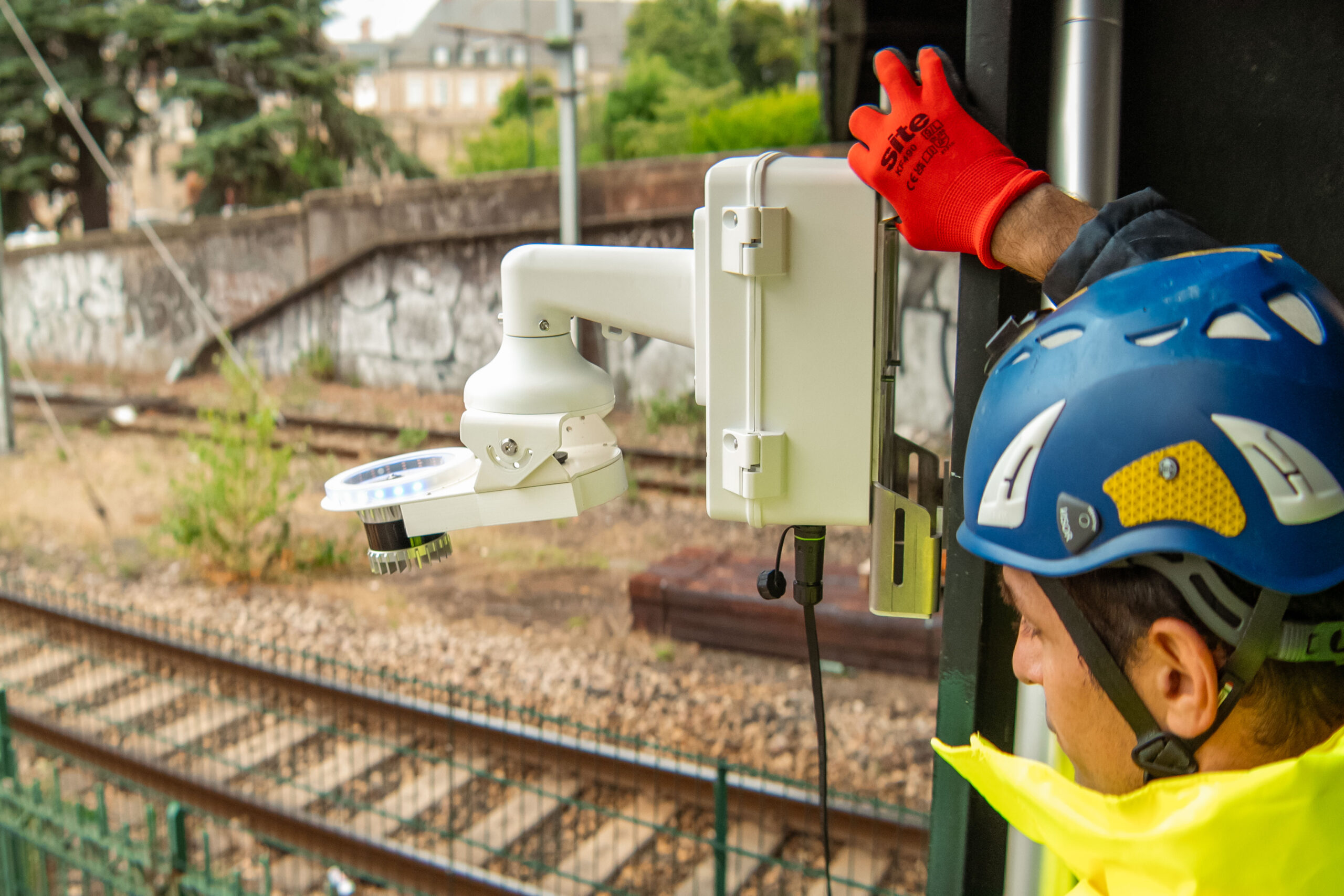 Man in yellow safety gear standing above railway tracks with an Inspemon monitoring machine