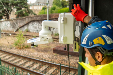 Man in yellow safety gear standing above railway tracks with an Inspemon monitoring machine