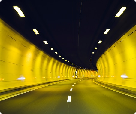 Illuminated tunnel with a roadway, showing lanes and lighting for safe passage.