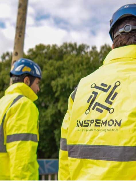 Two Inspemon employees wearing yellow safety outfits inside a workspace.